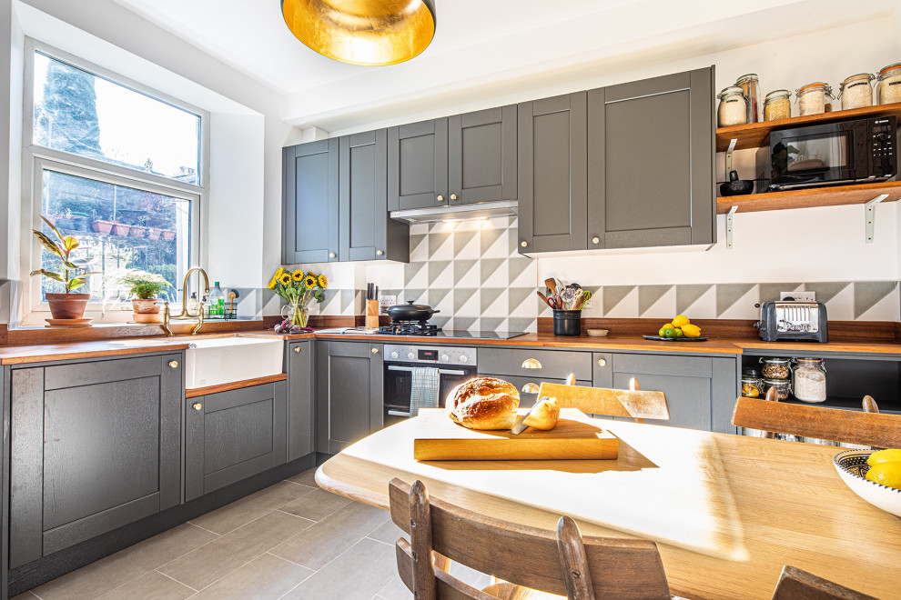 This is an example of a small classic l-shaped kitchen/diner in Other with a belfast sink, shaker cabinets, grey cabinets, wood worktops, grey splashback, integrated appliances, ceramic flooring, no island, grey floors and brown worktops.
