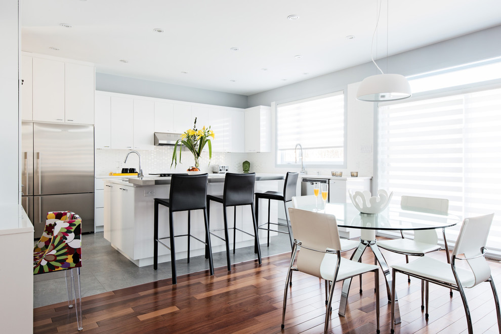 Inspiration pour une cuisine américaine design en L avec un placard à porte plane, des portes de placard blanches, une crédence blanche et un électroménager en acier inoxydable.