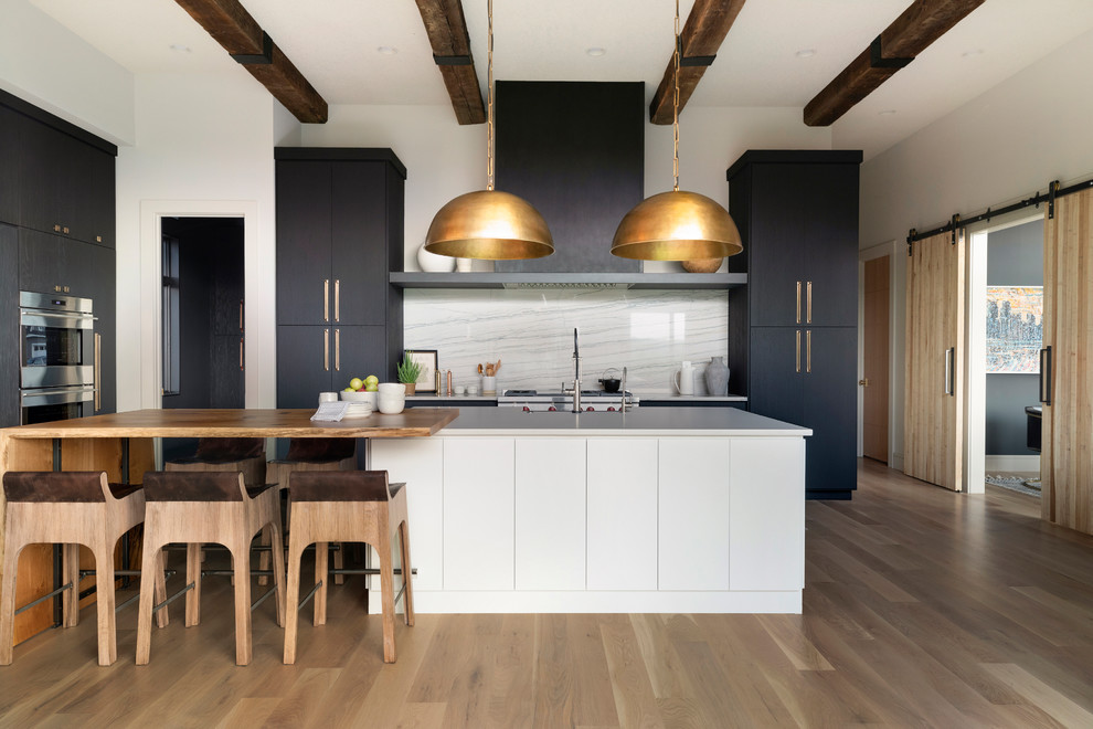 Moderne Wohnküche in L-Form mit flächenbündigen Schrankfronten, schwarzen Schränken, Küchenrückwand in Weiß, Küchengeräten aus Edelstahl, braunem Holzboden, Kücheninsel, braunem Boden und weißer Arbeitsplatte in Minneapolis