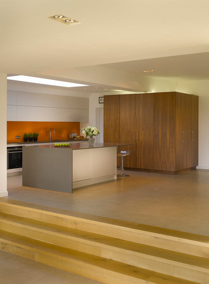 Large contemporary open plan kitchen in London with an island, flat-panel cabinets, white cabinets, orange splashback, glass sheet splashback and a submerged sink.