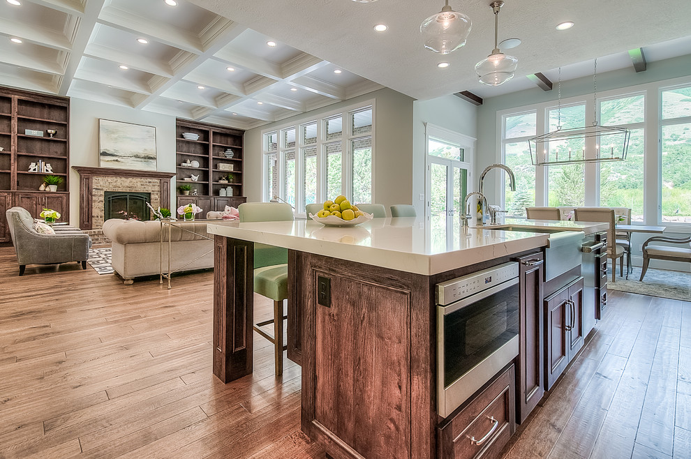 Design ideas for a large traditional l-shaped kitchen/diner in Salt Lake City with a belfast sink, shaker cabinets, dark wood cabinets, engineered stone countertops, white splashback, stone tiled splashback, stainless steel appliances, medium hardwood flooring and an island.