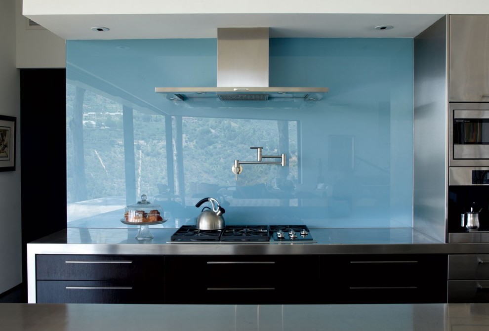 Пример оригинального дизайна: кухня в стиле модернизм с фасадами из нержавеющей стали, столешницей из нержавеющей стали, синим фартуком и фартуком из стекла