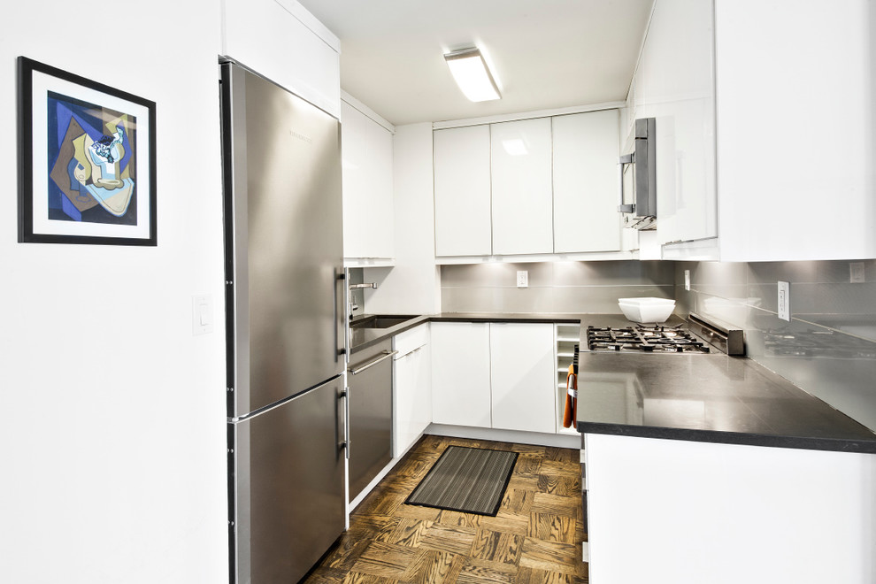 Small minimalist galley medium tone wood floor kitchen photo in New York with a drop-in sink, flat-panel cabinets, white cabinets, quartz countertops, gray backsplash, porcelain backsplash and stainless steel appliances