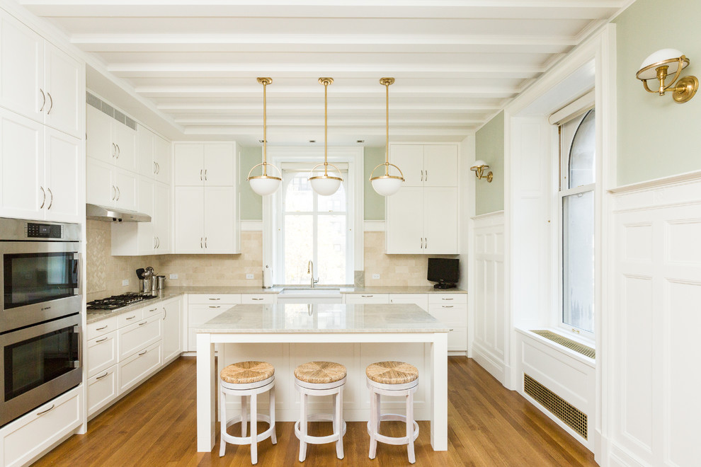 Geschlossene Klassische Küche in L-Form mit Landhausspüle, Schrankfronten im Shaker-Stil, weißen Schränken, Küchenrückwand in Beige, Küchengeräten aus Edelstahl, braunem Holzboden, Kücheninsel und braunem Boden in New York
