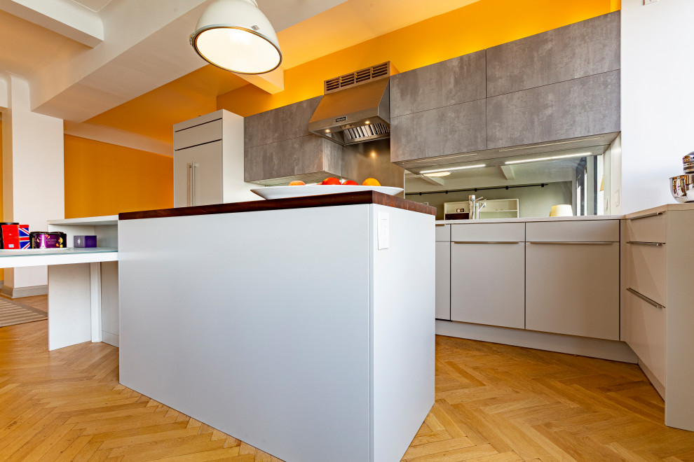 Photo of a medium sized contemporary u-shaped kitchen/diner in New York with a submerged sink, flat-panel cabinets, grey cabinets, engineered stone countertops, metallic splashback, mirror splashback, integrated appliances, light hardwood flooring, an island, beige floors and white worktops.