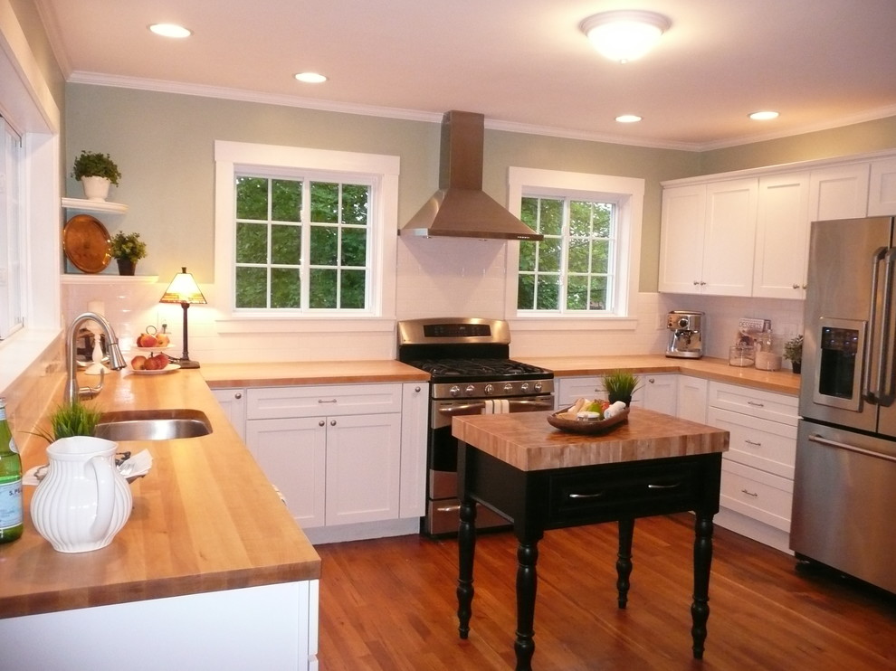 Mid-sized transitional u-shaped medium tone wood floor enclosed kitchen photo in Boston with an undermount sink, recessed-panel cabinets, white cabinets, wood countertops, white backsplash, subway tile backsplash, stainless steel appliances and no island