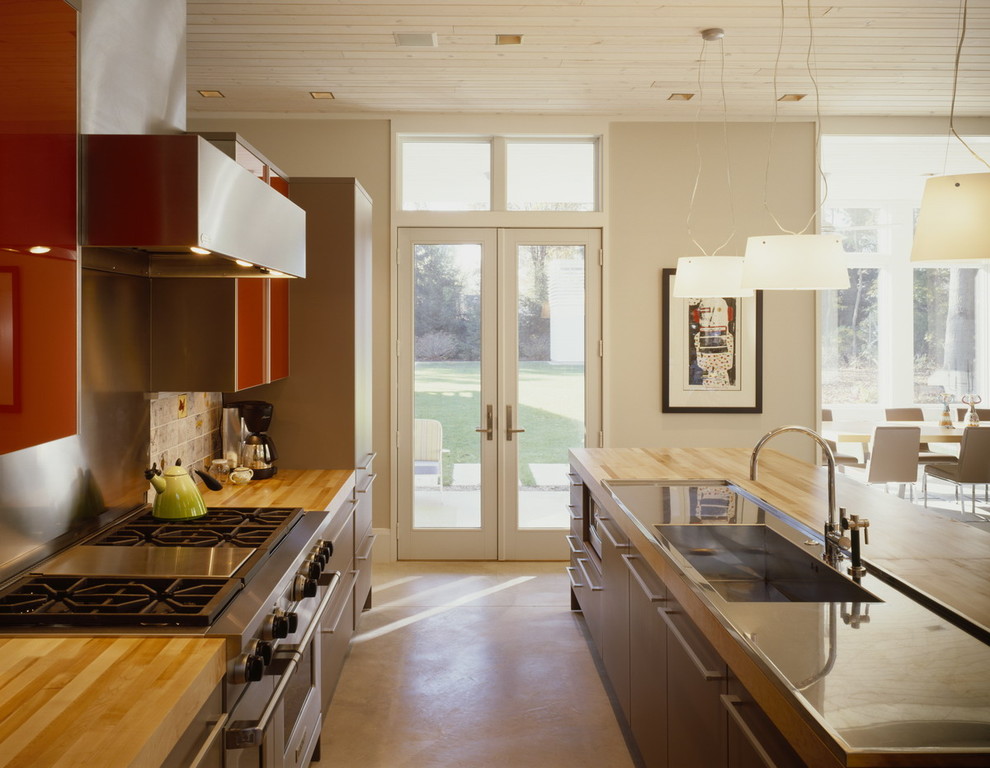 Inredning av ett modernt kök, med rostfria vitvaror, en integrerad diskho, släta luckor, röda skåp, stänkskydd med metallisk yta, stänkskydd i metallkakel och träbänkskiva