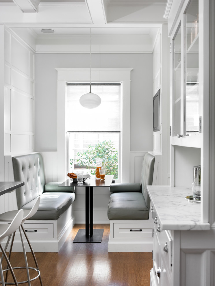 Cette photo montre une cuisine américaine grise et blanche chic avec des portes de placard blanches et un sol en bois brun.