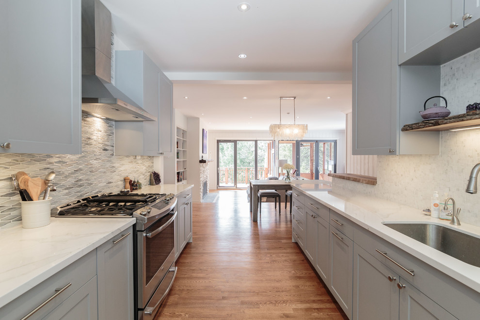 Inspiration for a mid-sized transitional galley medium tone wood floor and brown floor eat-in kitchen remodel in Montreal with an undermount sink, shaker cabinets, gray cabinets, quartz countertops, multicolored backsplash, stainless steel appliances, a peninsula and marble backsplash