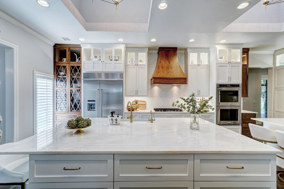 Large transitional medium tone wood floor and brown floor open concept kitchen photo in Oklahoma City with a farmhouse sink, shaker cabinets, white cabinets, quartzite countertops, white backsplash, porcelain backsplash, stainless steel appliances and two islands