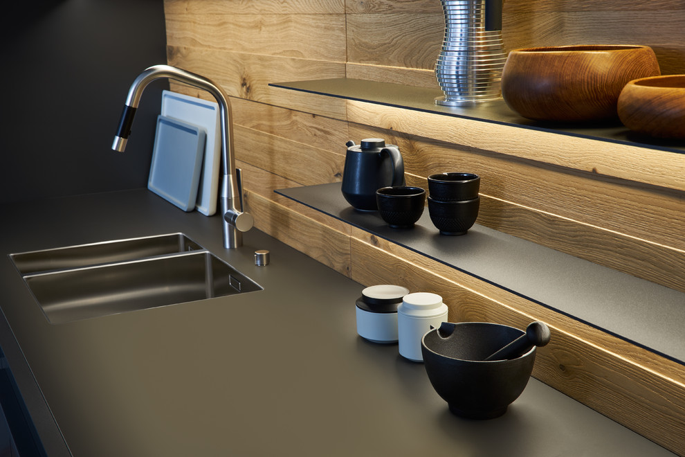 Esempio di una grande cucina moderna con lavello integrato, ante lisce, ante nere, paraspruzzi in legno, elettrodomestici neri e pavimento in cemento