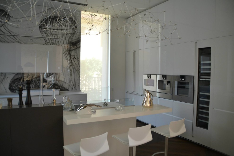 Moderne Wohnküche mit integriertem Waschbecken, weißen Schränken, Glas-Arbeitsplatte, Küchenrückwand in Weiß, Küchengeräten aus Edelstahl, braunem Holzboden und Kücheninsel in Sonstige