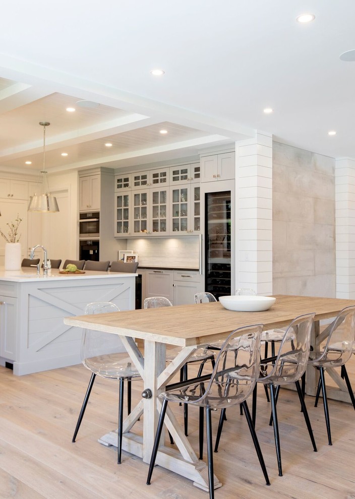 Enclosed kitchen - large transitional u-shaped light wood floor and brown floor enclosed kitchen idea in Vancouver with shaker cabinets, an island, a farmhouse sink, white cabinets, white backsplash, subway tile backsplash, stainless steel appliances and black countertops