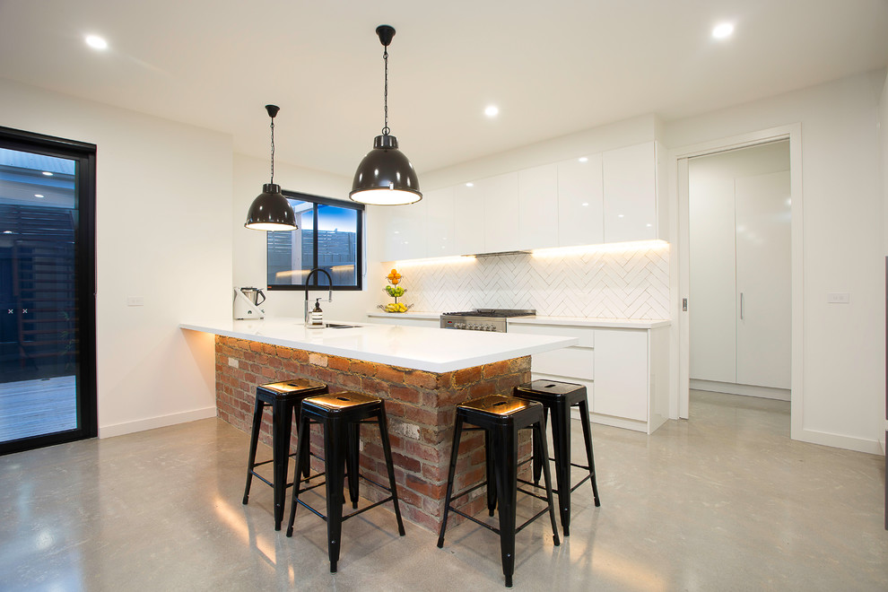 Example of a mid-sized trendy single-wall concrete floor and gray floor open concept kitchen design in Melbourne with an undermount sink, flat-panel cabinets, white cabinets, solid surface countertops, white backsplash, stainless steel appliances and a peninsula