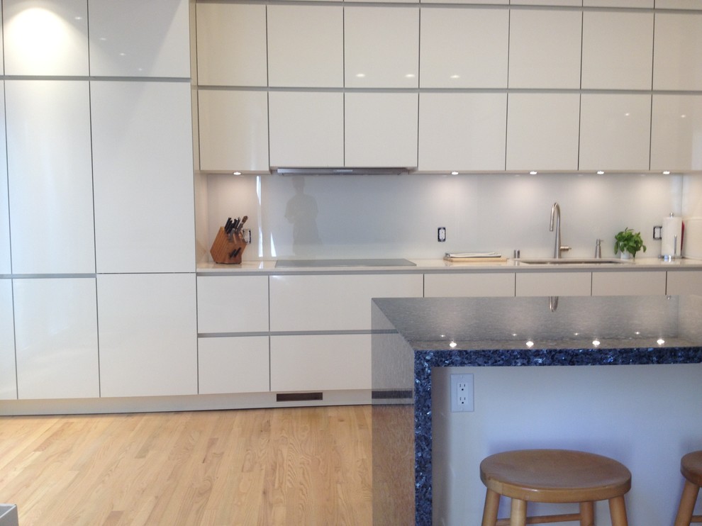 Medium sized contemporary single-wall kitchen/diner in San Francisco with a submerged sink, flat-panel cabinets, white cabinets, granite worktops, white splashback, glass sheet splashback, stainless steel appliances, light hardwood flooring and an island.