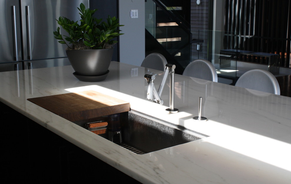 Example of a mid-sized minimalist l-shaped medium tone wood floor eat-in kitchen design in Minneapolis with an undermount sink, flat-panel cabinets, black cabinets, marble countertops, green backsplash, glass sheet backsplash, stainless steel appliances and an island