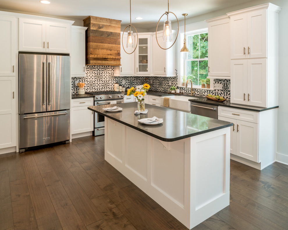Inspiration for a farmhouse l-shaped kitchen in Other with a belfast sink, shaker cabinets, white cabinets, multi-coloured splashback, stainless steel appliances, dark hardwood flooring, an island, brown floors and black worktops.
