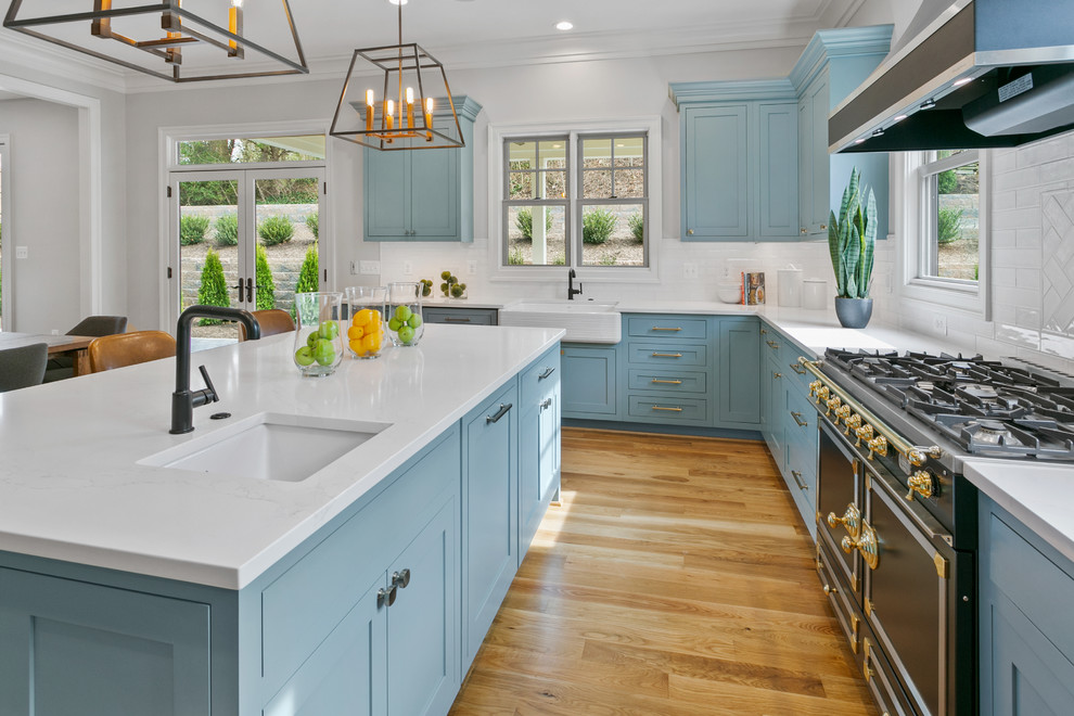 Esempio di una cucina design di medie dimensioni con lavello sottopiano, ante in stile shaker, ante blu, paraspruzzi bianco, elettrodomestici in acciaio inossidabile, pavimento in legno massello medio, pavimento marrone e top bianco