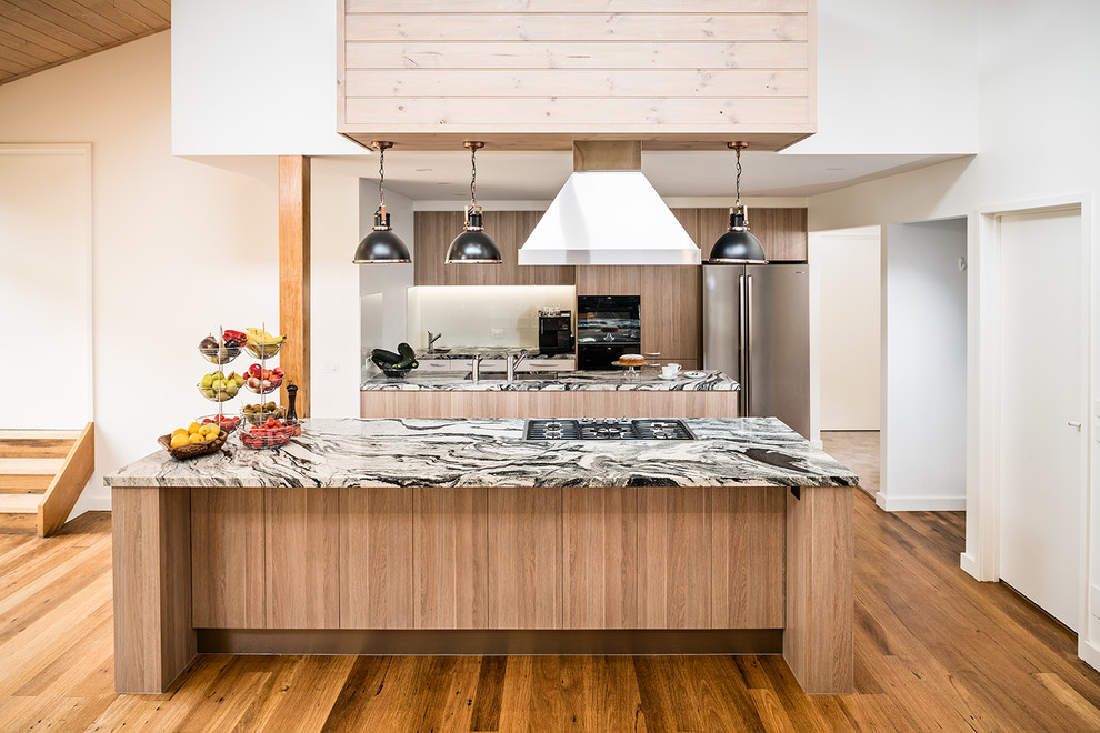 Inredning av ett modernt stort flerfärgad flerfärgat kök, med en undermonterad diskho, släta luckor, skåp i mellenmörkt trä, granitbänkskiva, vitt stänkskydd, glaspanel som stänkskydd, svarta vitvaror, mellanmörkt trägolv, flera köksöar och brunt golv