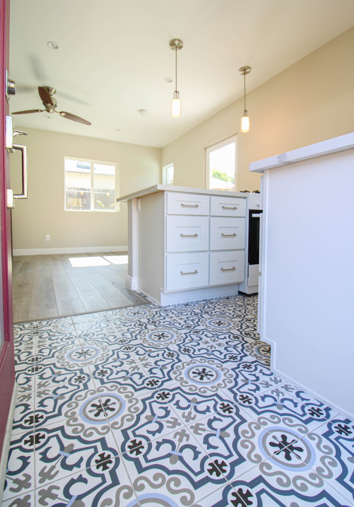 Foto på ett mellanstort funkis vit kök, med en nedsänkt diskho, luckor med infälld panel, vita skåp, vita vitvaror, en köksö, bänkskiva i kvarts, blått stänkskydd, stänkskydd i cementkakel, klinkergolv i keramik och vitt golv