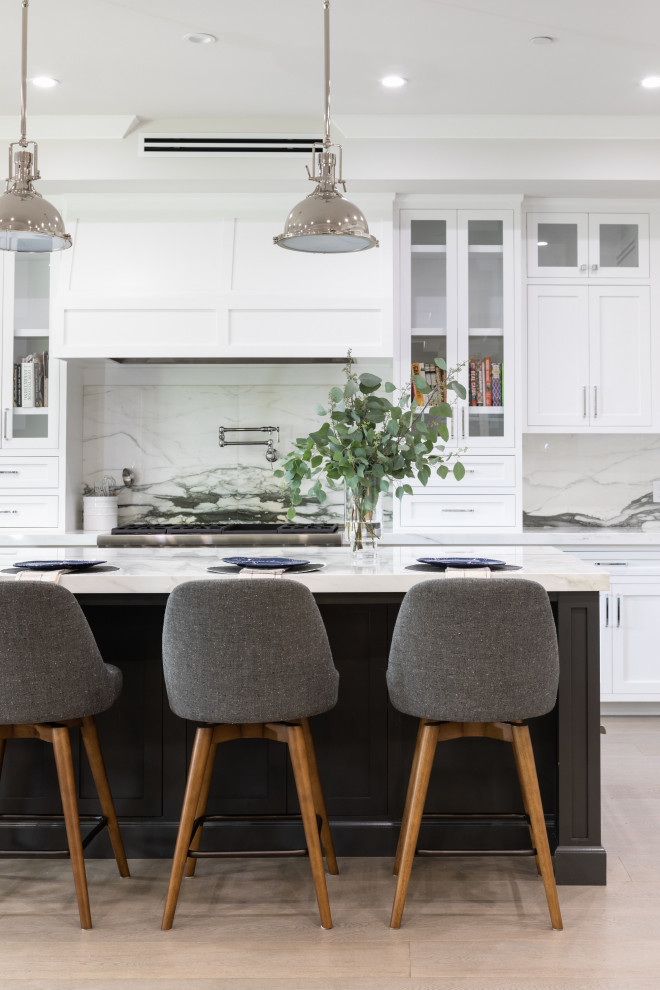 Inspiration for a large coastal u-shaped light wood floor and gray floor open concept kitchen remodel in Los Angeles with a farmhouse sink, shaker cabinets, white cabinets, marble countertops, white backsplash, marble backsplash, stainless steel appliances and an island