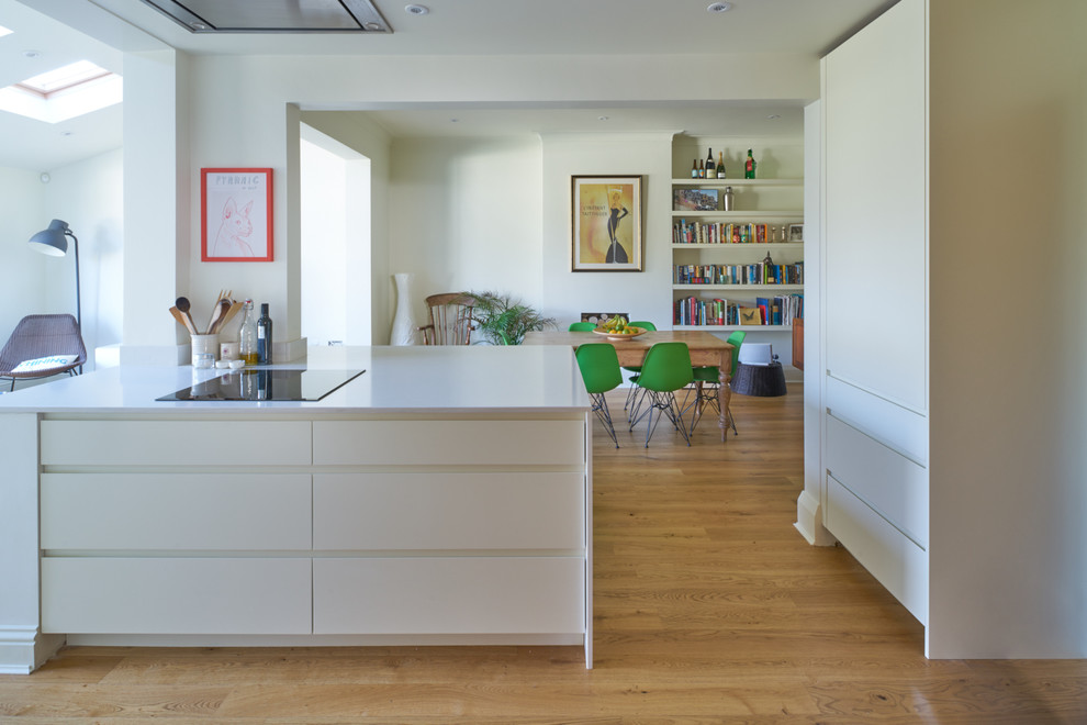 Medium sized contemporary u-shaped kitchen/diner in London with an integrated sink, flat-panel cabinets, white cabinets, white splashback, stainless steel appliances, medium hardwood flooring and no island.