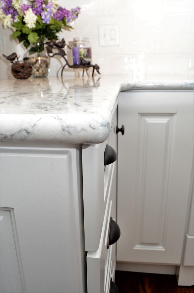 Bild på ett mellanstort vintage vit vitt kök, med en undermonterad diskho, luckor med upphöjd panel, vita skåp, bänkskiva i kvartsit, vitt stänkskydd, stänkskydd i tunnelbanekakel, rostfria vitvaror, mellanmörkt trägolv och brunt golv