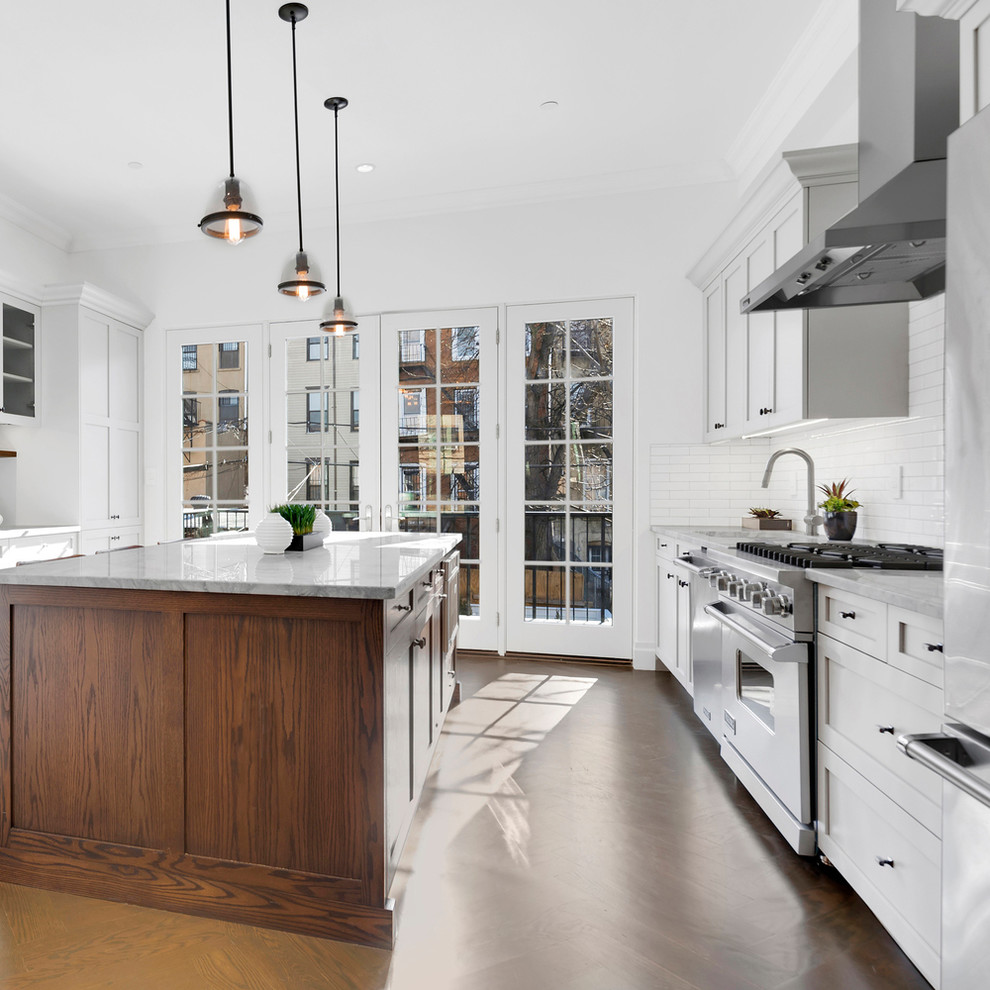 Zweizeilige Klassische Küche mit Unterbauwaschbecken, Schrankfronten im Shaker-Stil, weißen Schränken, Küchenrückwand in Weiß, Küchengeräten aus Edelstahl, braunem Holzboden, Kücheninsel, braunem Boden und grauer Arbeitsplatte in New York