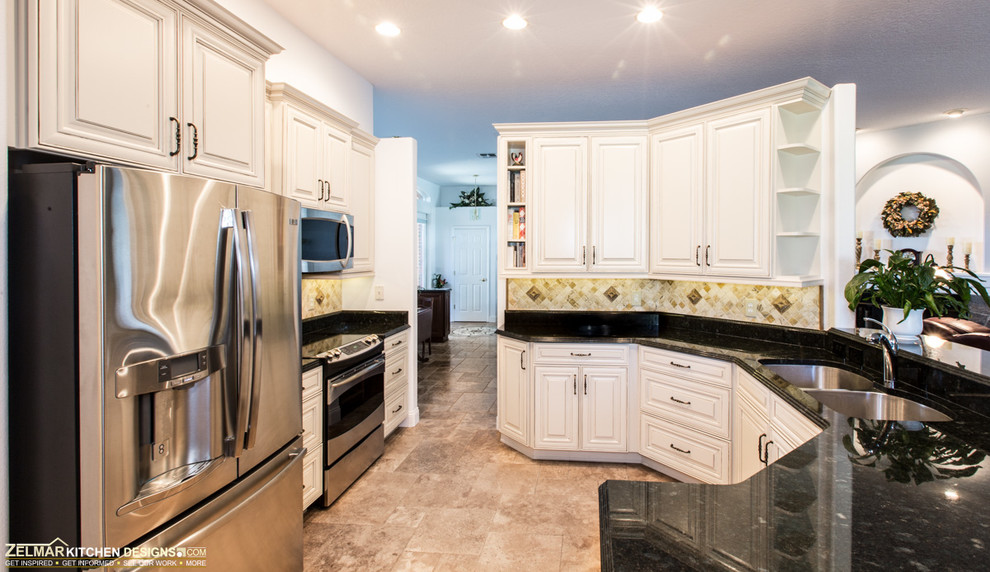 Inredning av ett klassiskt kök, med en undermonterad diskho, luckor med upphöjd panel, vita skåp, granitbänkskiva, vitt stänkskydd, stänkskydd i stenkakel, rostfria vitvaror, travertin golv och en halv köksö