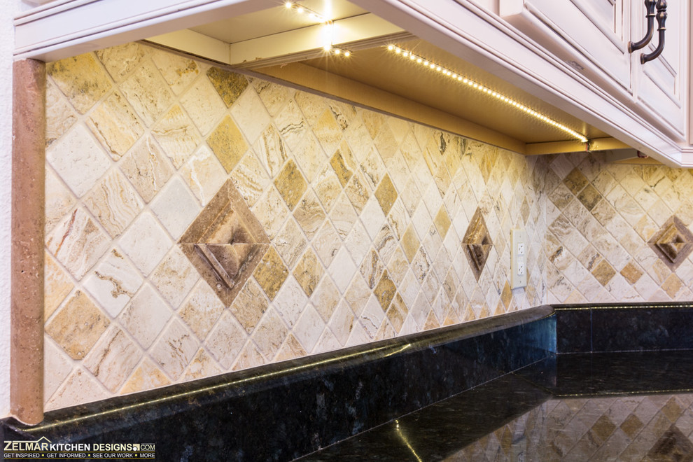 Exempel på ett klassiskt kök, med en undermonterad diskho, luckor med upphöjd panel, vita skåp, granitbänkskiva, vitt stänkskydd, stänkskydd i stenkakel, rostfria vitvaror, travertin golv och en halv köksö
