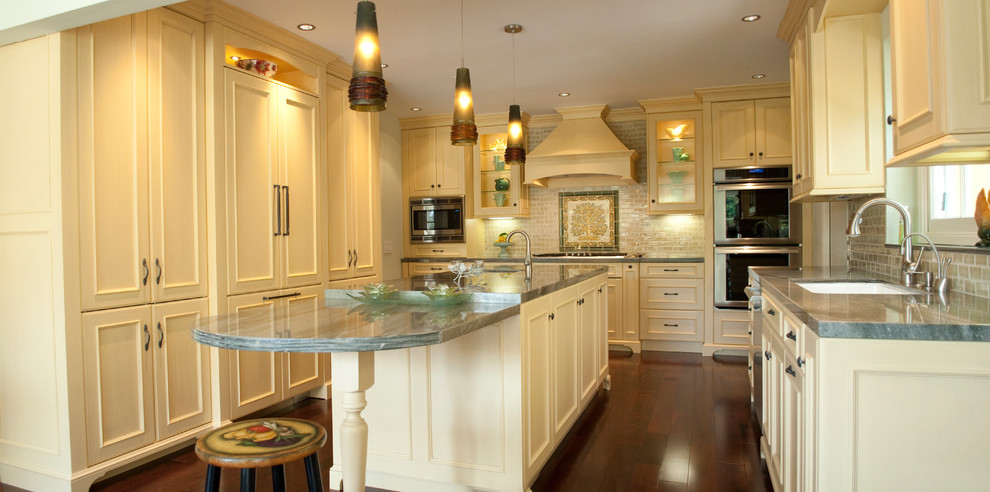 Exempel på ett mellanstort klassiskt kök, med gula skåp, granitbänkskiva, grönt stänkskydd, stänkskydd i keramik, rostfria vitvaror, mellanmörkt trägolv, en köksö, en undermonterad diskho, luckor med profilerade fronter och brunt golv