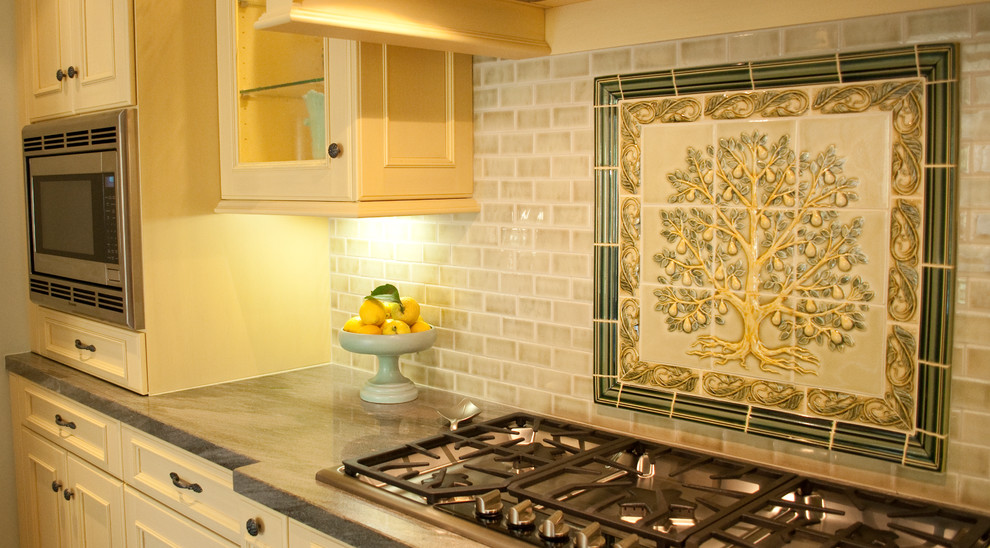 Klassisk inredning av ett mellanstort kök, med gula skåp, granitbänkskiva, grönt stänkskydd, stänkskydd i keramik, rostfria vitvaror, mellanmörkt trägolv, en köksö, en undermonterad diskho, luckor med profilerade fronter och brunt golv