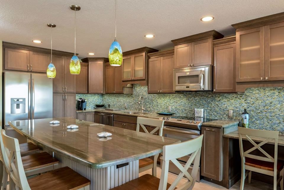 This is an example of a large coastal l-shaped open plan kitchen in Tampa with a double-bowl sink, shaker cabinets, medium wood cabinets, granite worktops, blue splashback, glass tiled splashback, stainless steel appliances, an island and beige floors.