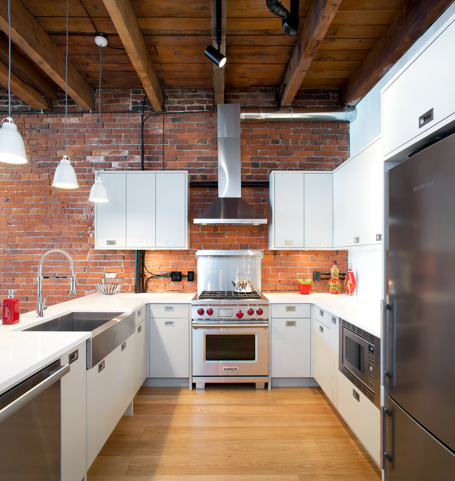 Foto de cocinas en U industrial sin isla con fregadero sobremueble, armarios con paneles lisos, puertas de armario blancas, electrodomésticos de acero inoxidable y suelo de madera clara