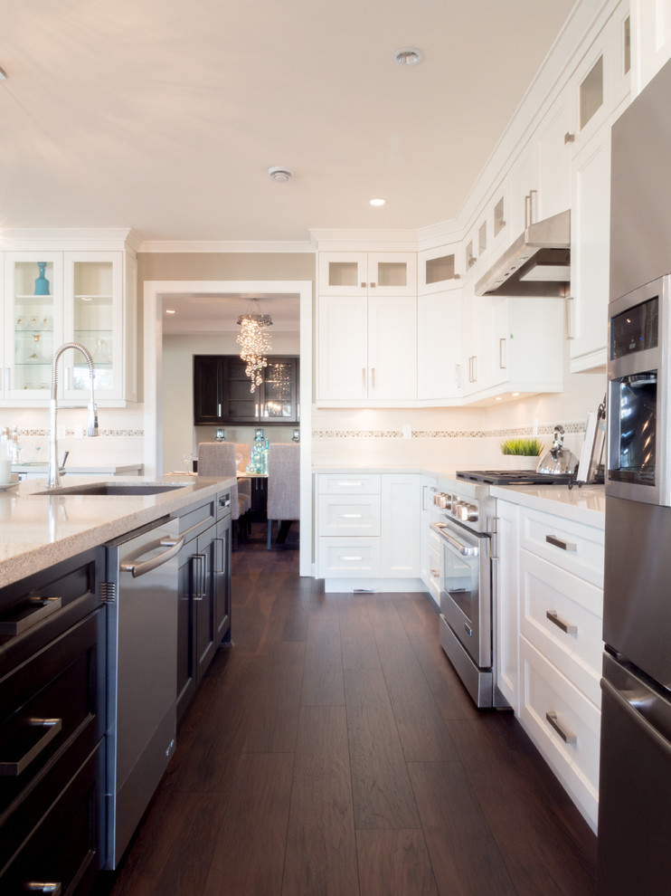 Bild på ett mellanstort funkis kök, med en undermonterad diskho, luckor med infälld panel, vita skåp, bänkskiva i kvarts, vitt stänkskydd, stänkskydd i mosaik, rostfria vitvaror, mörkt trägolv och en köksö