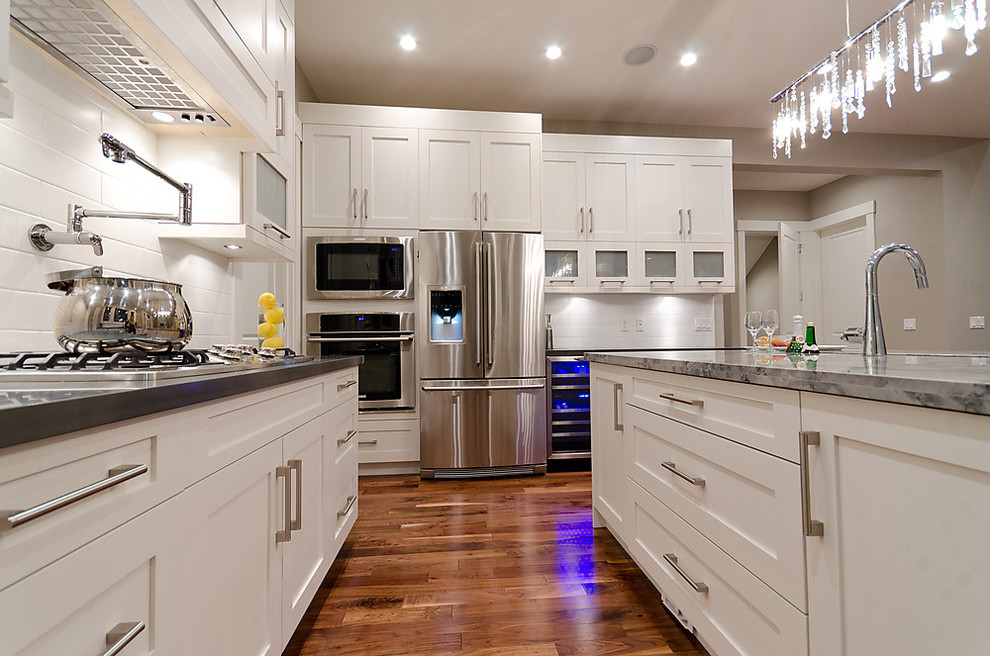 Example of a mid-sized transitional u-shaped medium tone wood floor eat-in kitchen design in Vancouver with an undermount sink, shaker cabinets, white cabinets, quartzite countertops, white backsplash, subway tile backsplash, stainless steel appliances and an island