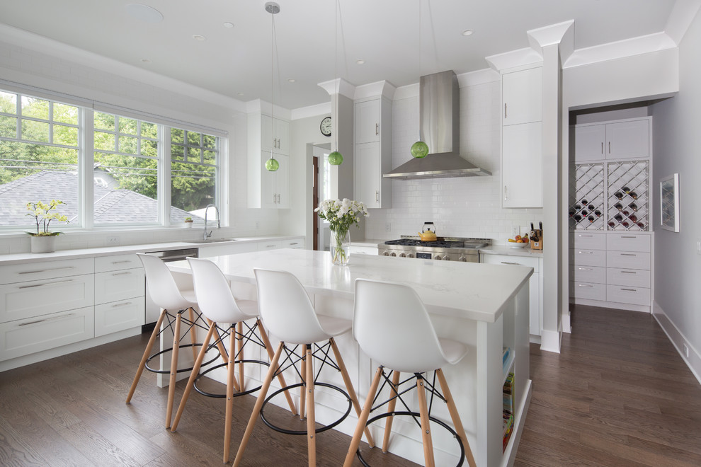 Example of a mid-sized transitional u-shaped medium tone wood floor and brown floor open concept kitchen design in Vancouver with an undermount sink, shaker cabinets, white cabinets, quartz countertops, white backsplash, subway tile backsplash, stainless steel appliances, an island and white countertops