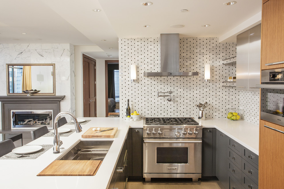 На фото: п-образная, серо-белая кухня-гостиная в современном стиле с врезной мойкой, серыми фасадами, разноцветным фартуком и техникой из нержавеющей стали с