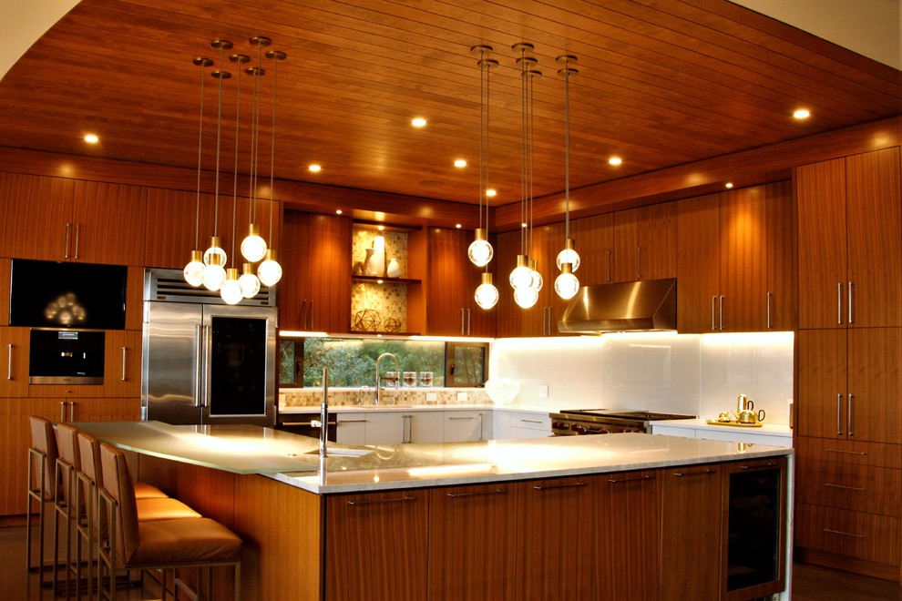 Exempel på ett mycket stort modernt vit vitt kök, med en undermonterad diskho, släta luckor, skåp i rostfritt stål, bänkskiva i glas, vitt stänkskydd, glaspanel som stänkskydd, rostfria vitvaror, betonggolv, en köksö och grått golv