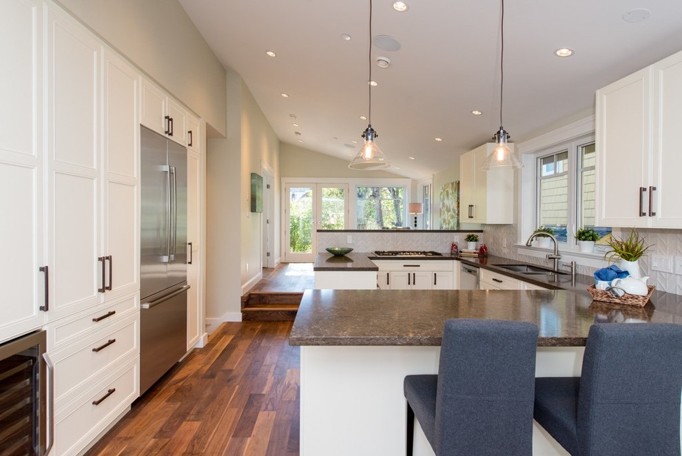 Large modern u-shaped open plan kitchen in Vancouver with a submerged sink, shaker cabinets, white cabinets, engineered stone countertops, white splashback, ceramic splashback, stainless steel appliances, laminate floors, multiple islands and brown floors.