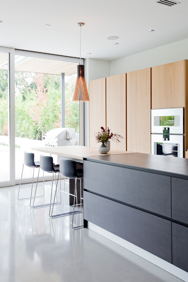 Moderne Küche mit flächenbündigen Schrankfronten, hellbraunen Holzschränken, Küchengeräten aus Edelstahl, Betonboden und Kücheninsel in Vancouver