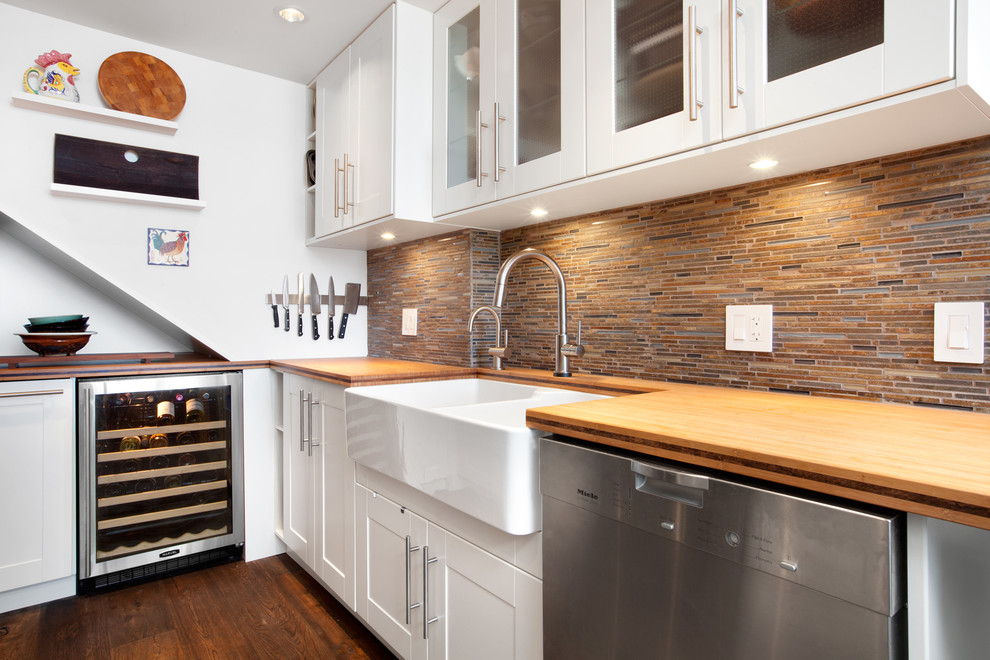 Inspiration for a transitional galley enclosed kitchen remodel in Vancouver with a farmhouse sink, shaker cabinets, white cabinets, wood countertops, brown backsplash, matchstick tile backsplash and stainless steel appliances