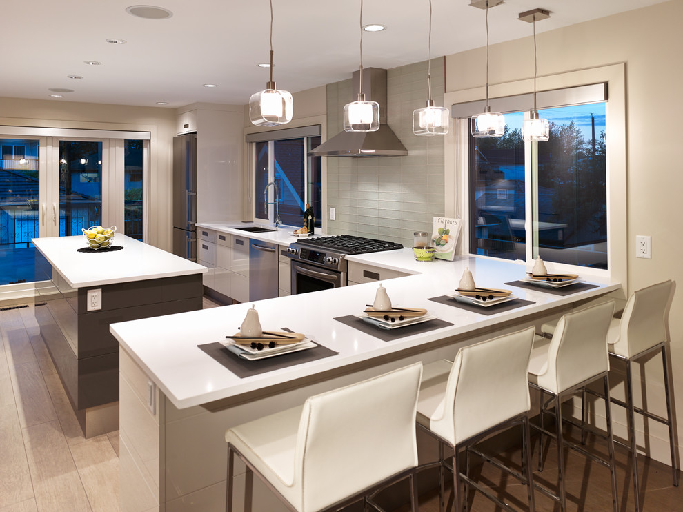 Design ideas for a contemporary l-shaped kitchen in Vancouver with flat-panel cabinets, stainless steel appliances, white cabinets, glass tiled splashback and white splashback.