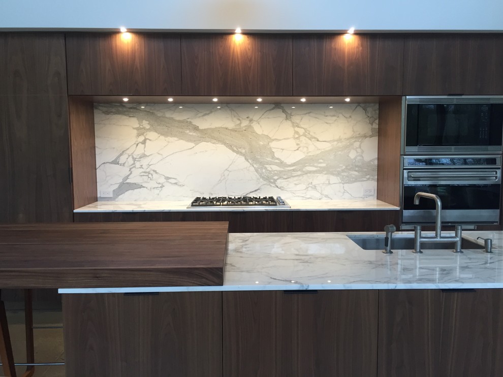 Inspiration for a large modern concrete floor open concept kitchen remodel in New York with an undermount sink, flat-panel cabinets, brown cabinets, marble countertops, white backsplash, stone slab backsplash, stainless steel appliances and an island