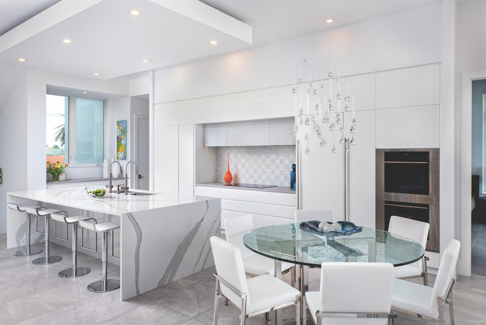 Photo of a contemporary kitchen/diner in Atlanta with a triple-bowl sink, flat-panel cabinets, white cabinets, white splashback, stainless steel appliances, an island, grey floors and grey worktops.
