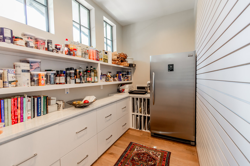 This is an example of a contemporary l-shaped kitchen pantry in Houston with flat-panel cabinets, white cabinets, stainless steel appliances, medium hardwood flooring, no island, brown floors and white worktops.