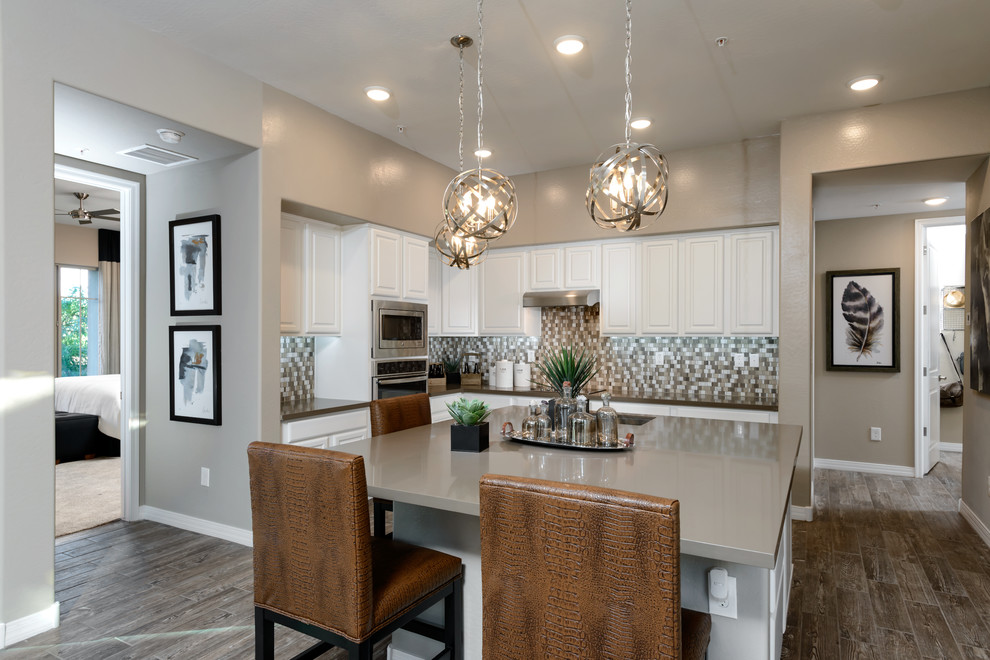 Mid-sized trendy l-shaped ceramic tile open concept kitchen photo in Phoenix with an undermount sink, raised-panel cabinets, white cabinets, quartz countertops, multicolored backsplash, glass tile backsplash, stainless steel appliances and an island