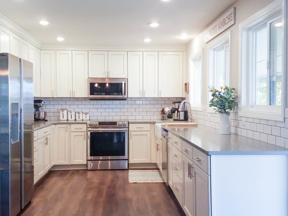 Mid-sized cottage u-shaped vinyl floor and brown floor eat-in kitchen photo in Seattle with a farmhouse sink, recessed-panel cabinets, white cabinets, quartz countertops, white backsplash, subway tile backsplash, stainless steel appliances and no island