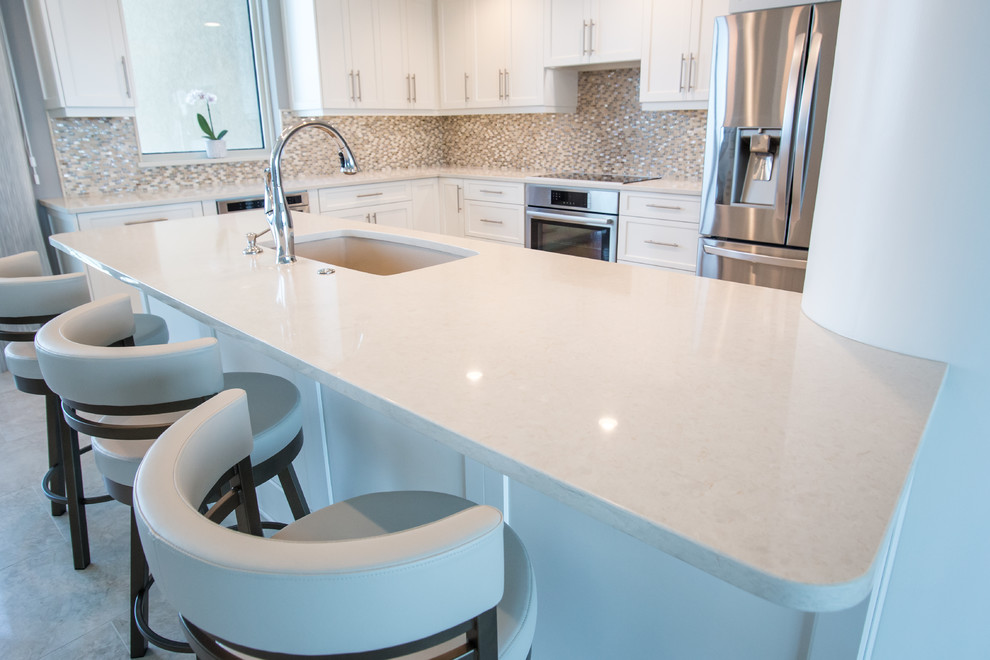 Open concept kitchen - mid-sized contemporary l-shaped travertine floor open concept kitchen idea in Miami with an undermount sink, shaker cabinets, white cabinets, quartz countertops, multicolored backsplash, glass tile backsplash, stainless steel appliances and a peninsula