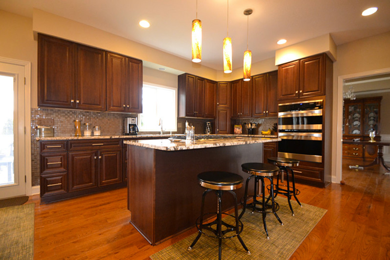 Example of a mid-sized classic l-shaped medium tone wood floor eat-in kitchen design in Columbus with an undermount sink, raised-panel cabinets, dark wood cabinets, granite countertops, metallic backsplash, glass tile backsplash, stainless steel appliances and an island